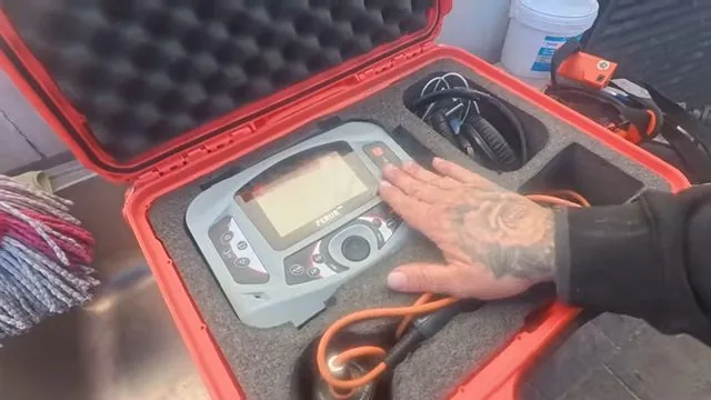 A hand on a handheld leak detector sitting in a red hard case with cables coiled beside it