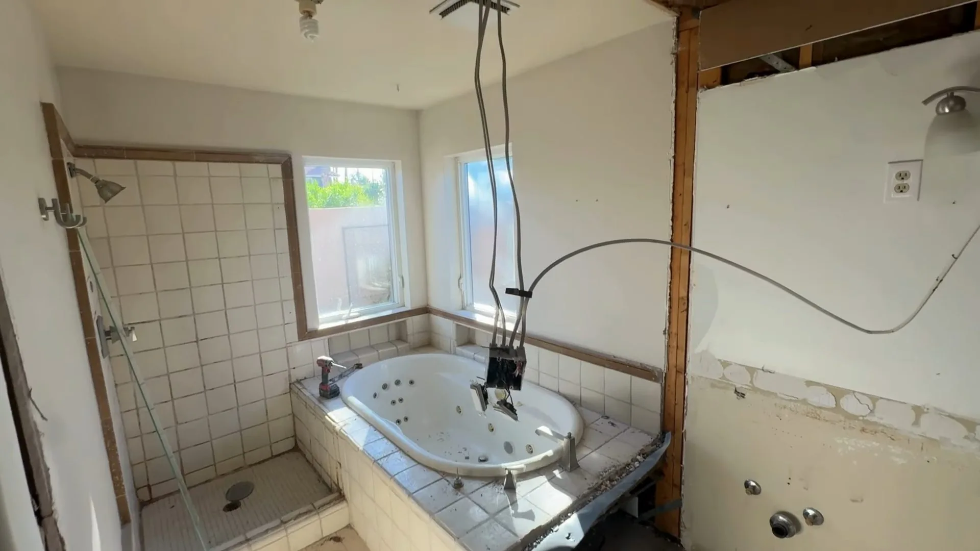 A bathroom with the walls opened up, a built-in tub and a shower stall with tile still on one side