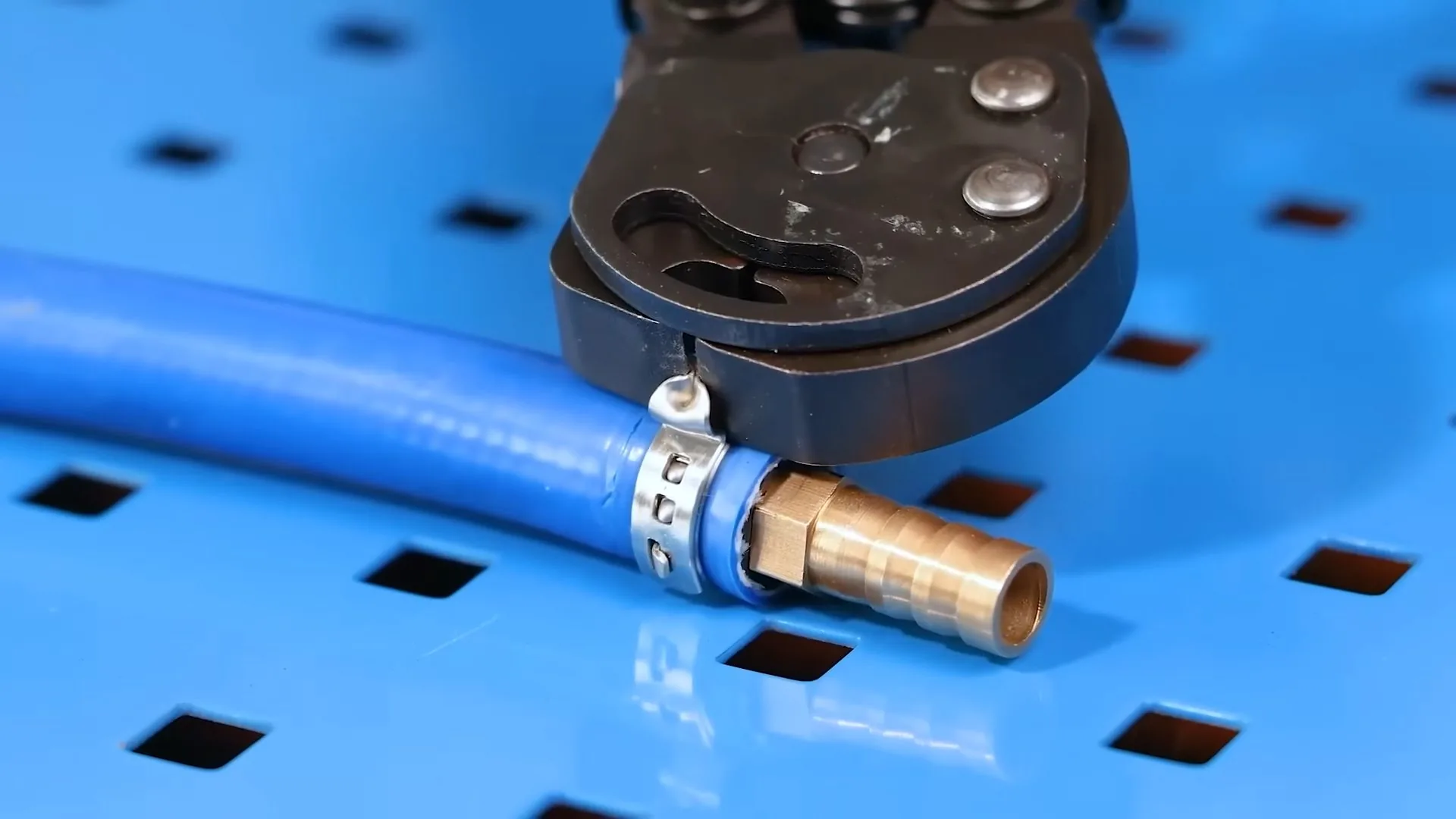 A length of blue PEX tubing with a brass fitting and a crimp tool resting on a blue perforated bench
