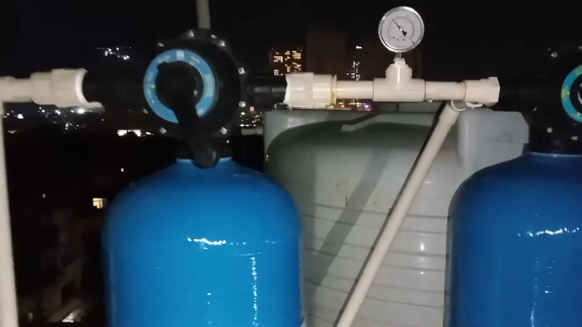 Two blue pressure tanks joined by white pipe with a pressure gauge and bypass valves, photographed at night
