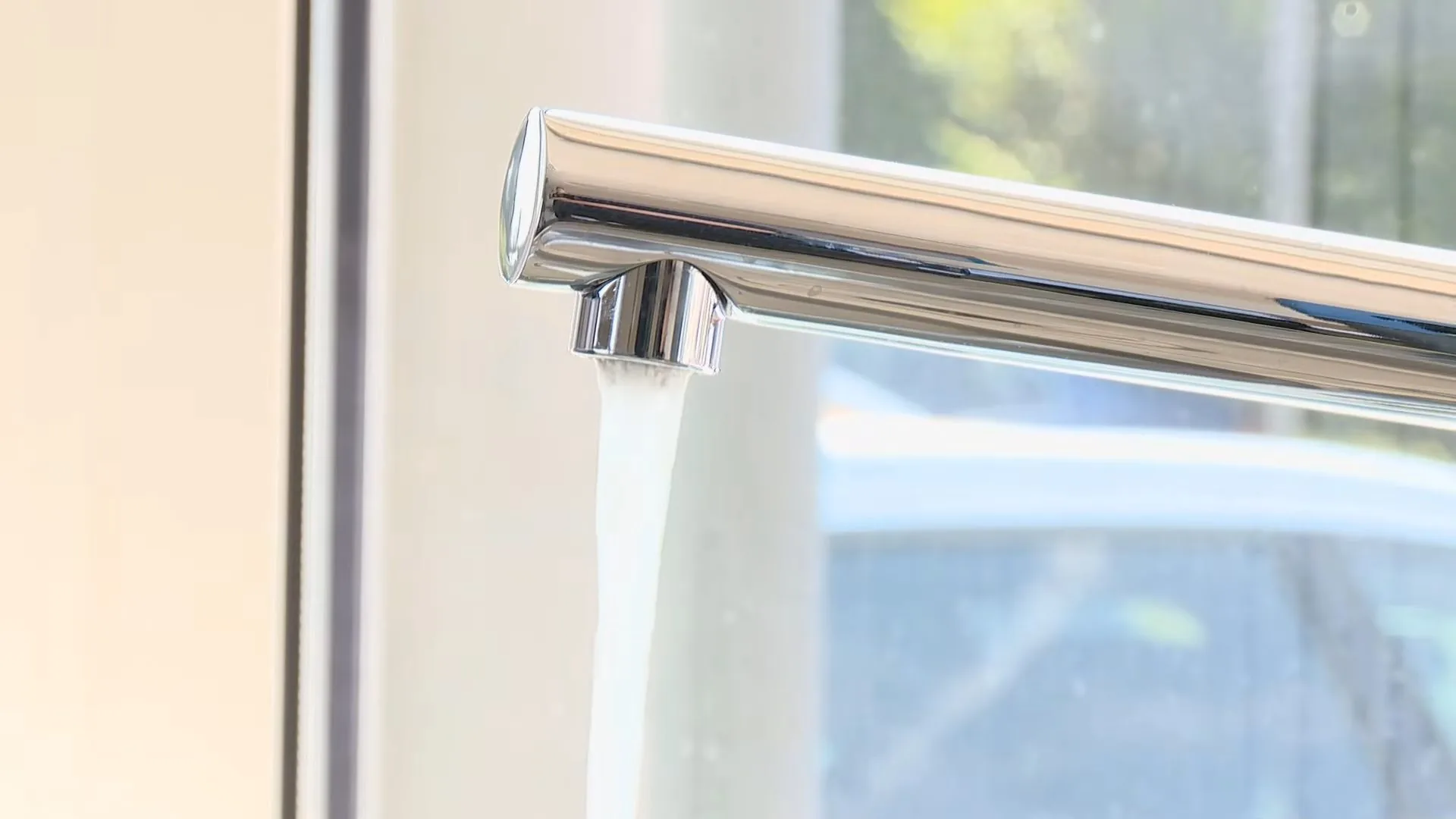 A chrome faucet spout running a stream of water in front of a bright window