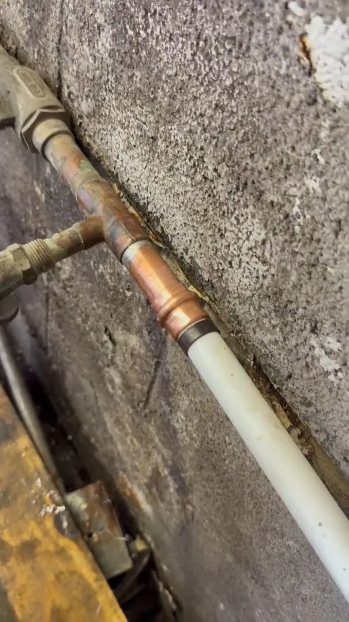 A copper water line running along a concrete wall and into a cut opening in the floor