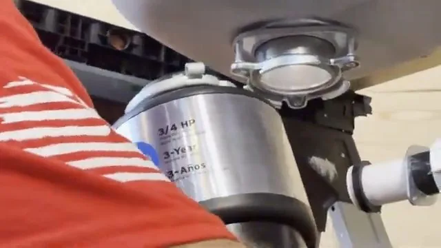 A stainless garbage disposal being lifted up against the mounting ring below a sink basin