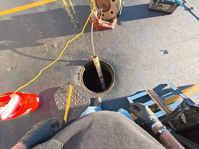 Top-down view of a technician feeding a drain cable into a round drain opening in a paved floor
