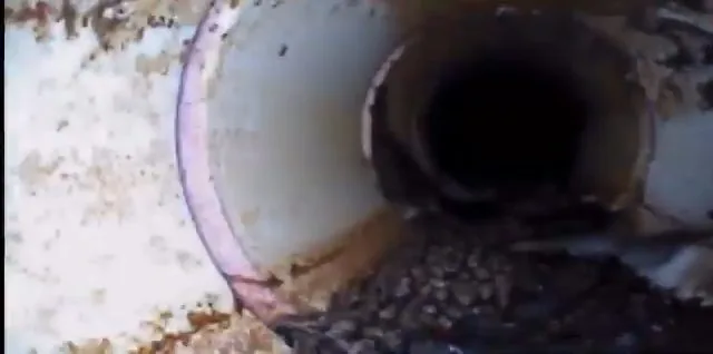 A camera view down a white pipe with a joint and some gravel sitting at the bottom
