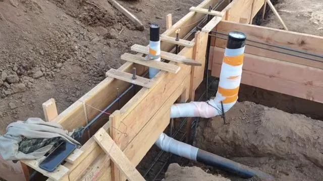 Wood forms for a new foundation with white and black plumbing stubs sleeved through the footing