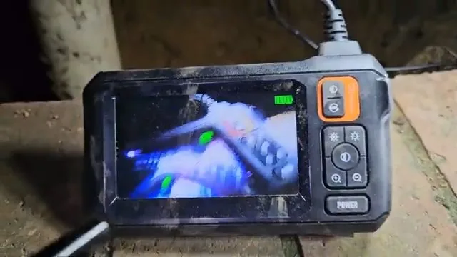 A handheld inspection monitor on a wooden surface showing the inside of a pipe in blue and white