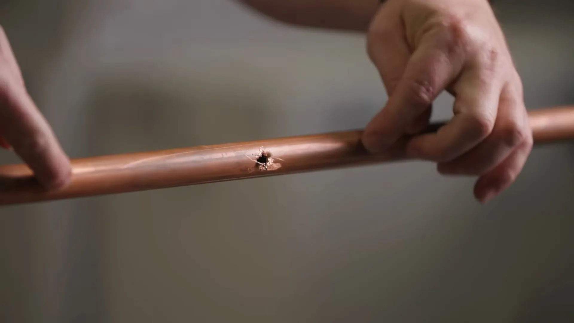 Two hands holding a length of copper pipe that has a small pinhole in its wall