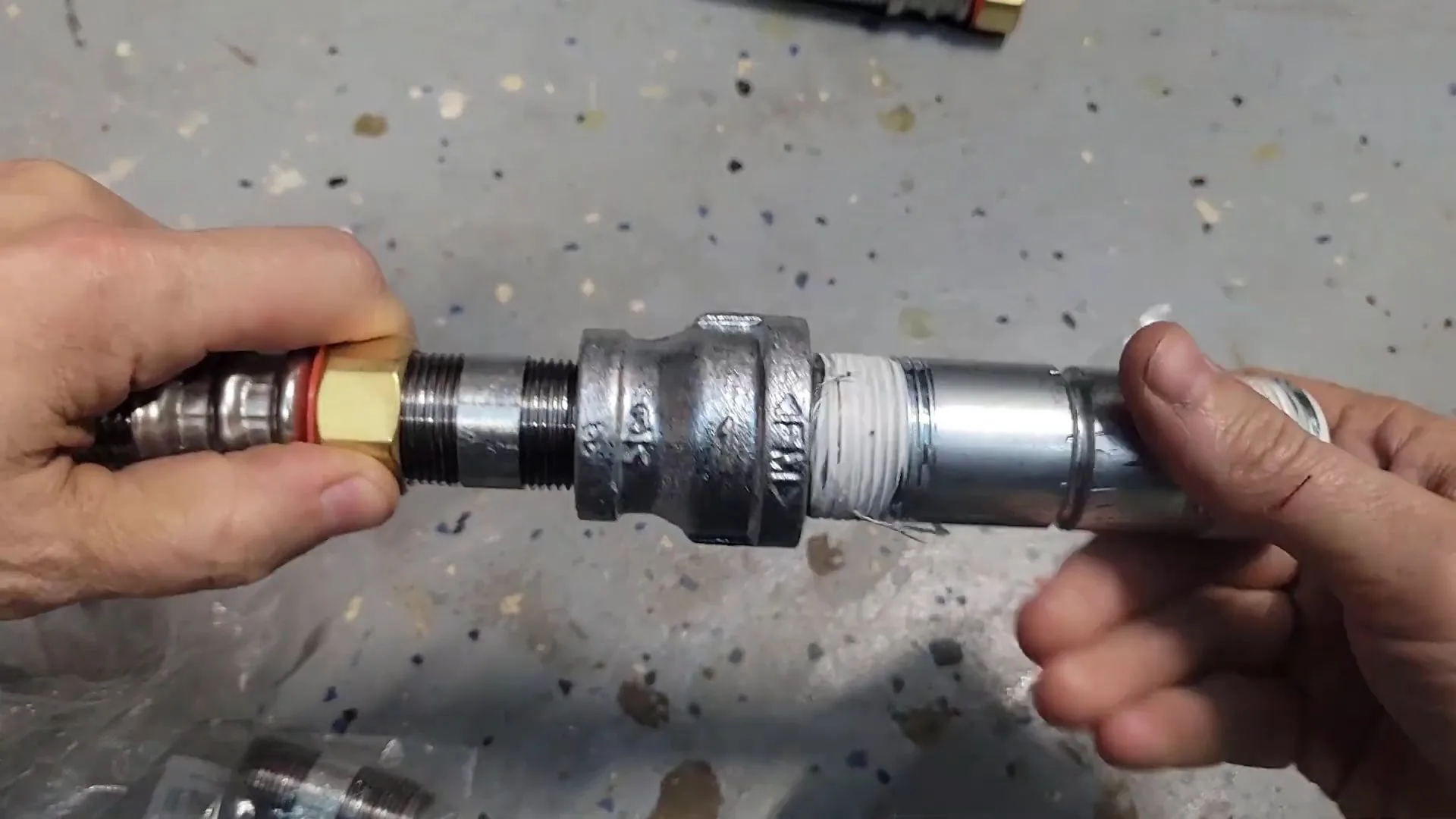 Two hands joining threaded steel pipe fittings with a brass quick coupling on the left end