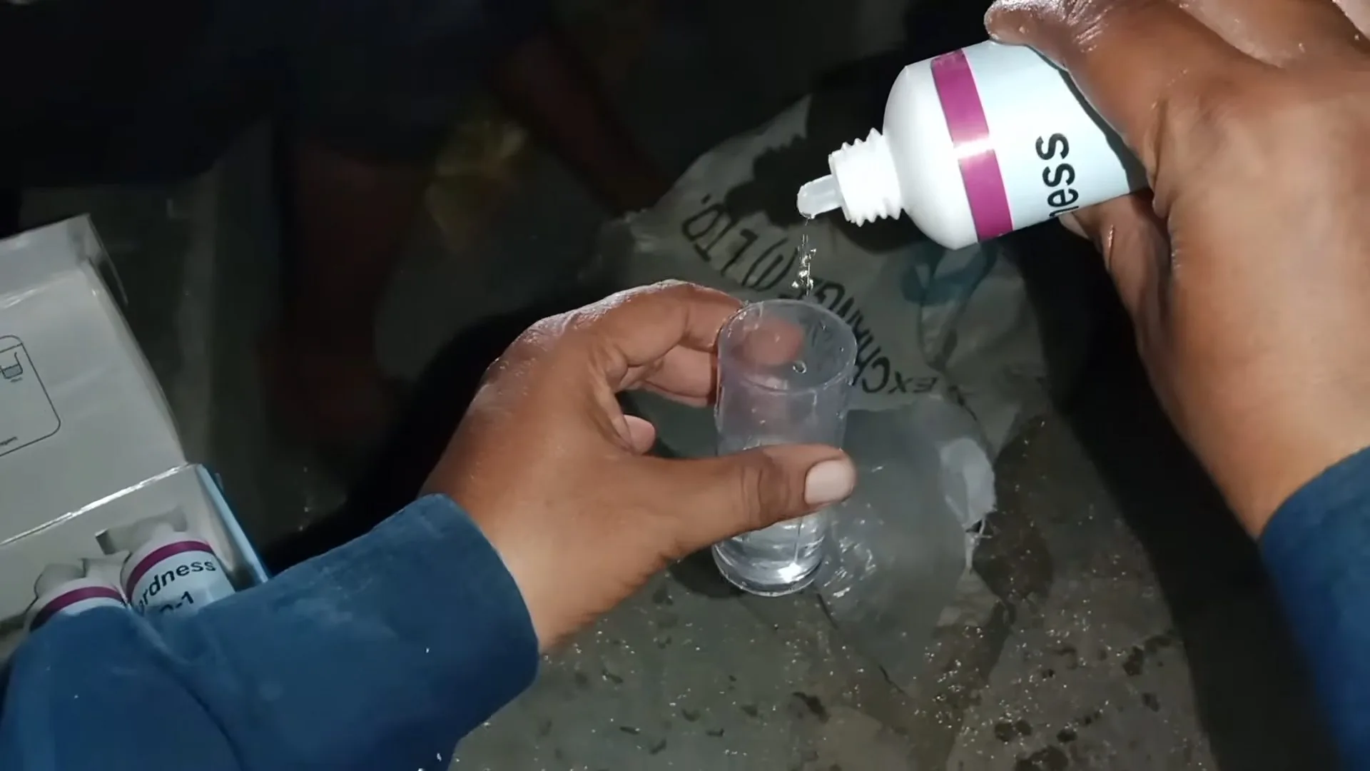 A hand holding a small bottle over a clear vial of water while another hand holds the vial