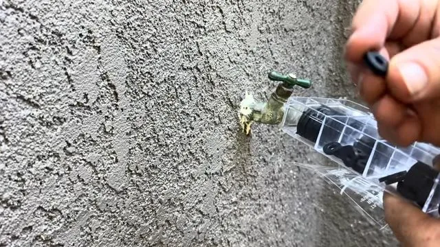 A brass outdoor hose bib on a stucco wall with water running down from the base of the spout