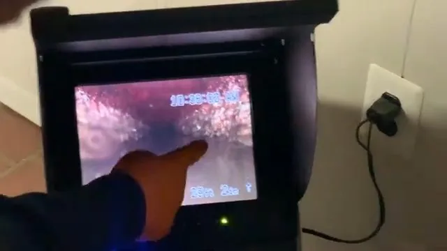 A hand pointing at a small monitor showing the pink inside of a pipe during a camera inspection