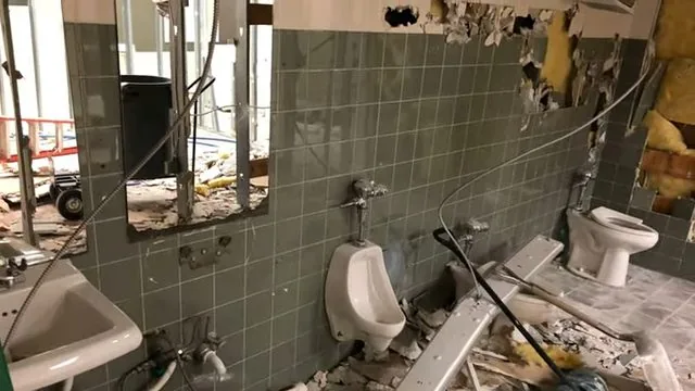 A restroom with tile walls, wall-hung urinals and exposed supply and drain work during a renovation