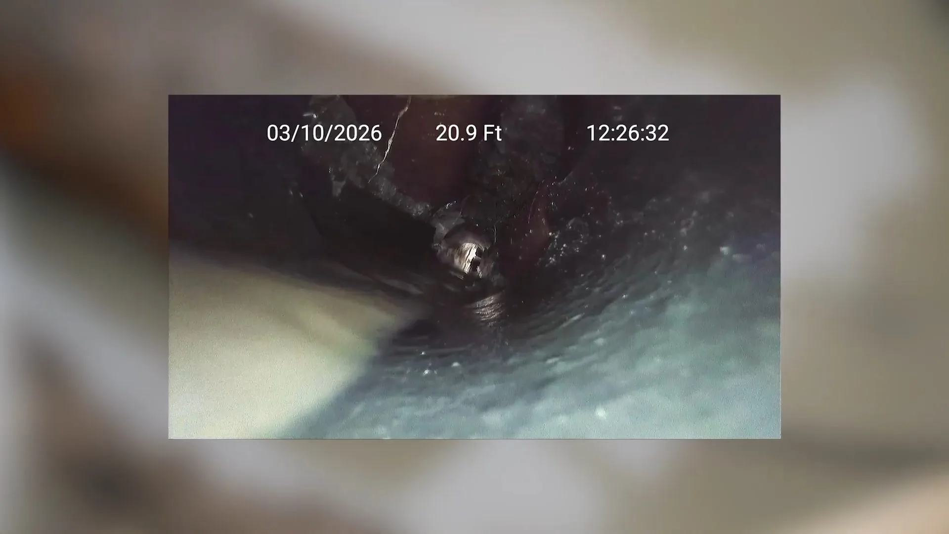 A sewer camera monitor with a timestamp showing the dark inside of an old drain pipe
