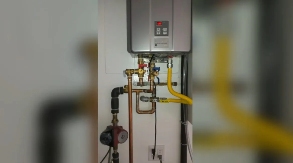 A tankless water heater on a wall with a yellow gas connector and a set of valves and pipes below it
