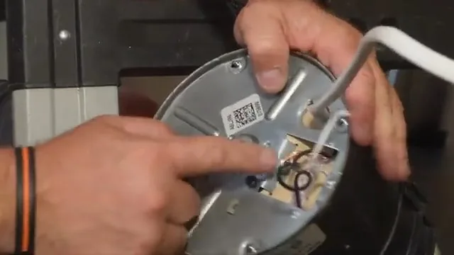 A hand pointing at the underside plate of a garbage disposal while another hand holds the unit steady