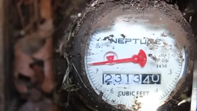 Close view of a round water meter dial with a red sweep hand and a row of digits