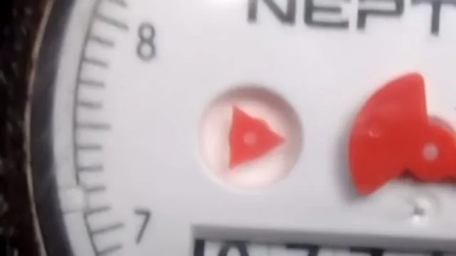 Close view of a water meter dial with a red triangular flow indicator and a red sweep hand
