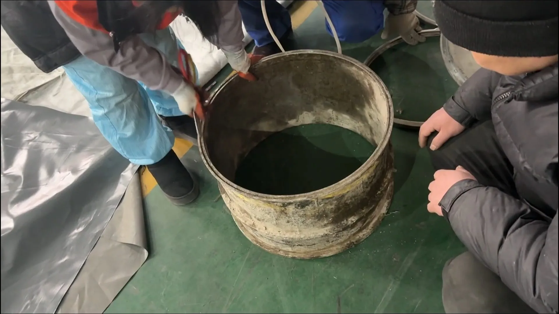 Workers handling a barrel of dark water on plastic sheeting laid over a floor